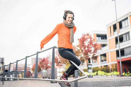 Portrait of laughing woman with cordless headphones sliding down a banister photo