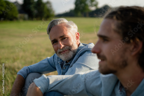 Mature father with adult son sitting on a meadow in the countryside