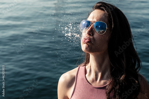 Portrait of young woman wearing sunglasses snorting water photo