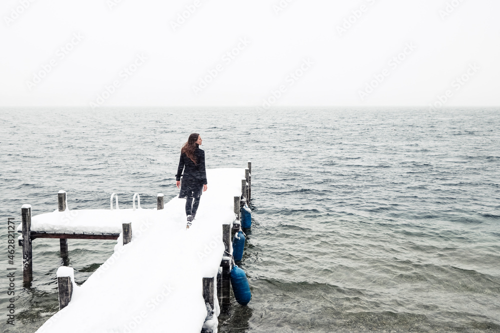 Back view of young woman walking on snow-covered jetty at Lake Starnberg, Germany Back view of young woman walking on snow-covered jetty at Lake Starnberg, Germany