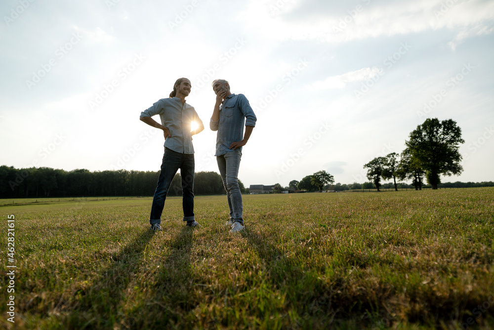 Father and adult son standing on a meadow in the countryside at sunset Father and adult son standing on a meadow in the countryside at sunset
