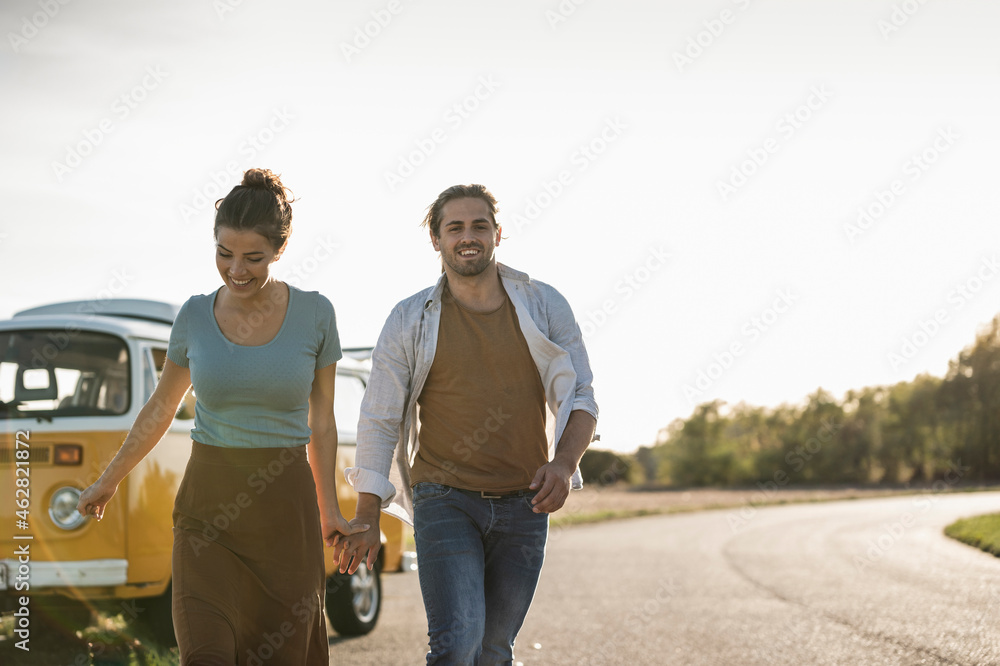 Happy couple doing a road trip with a camper, holding hands on the road Happy couple doing a road trip with a camper, holding hands on the road