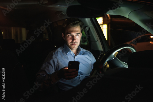 Young man using cell phone in car at night photo