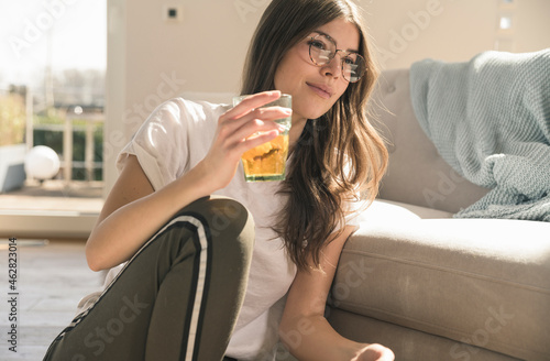 Young woman sitting on the floor at home with a drink