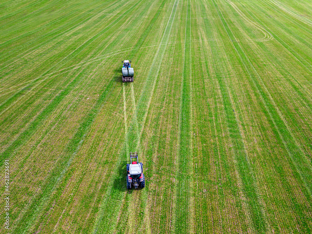 Aerial view of two tractors collecting hay bales in field Aerial view of two tractors collecting hay bales in field