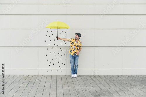 Digital composite of young man holding an umbrella at a wall with raindrops photo
