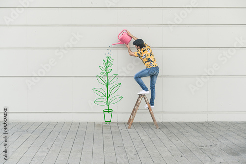Digital composite of young man watering flower at a wall photo