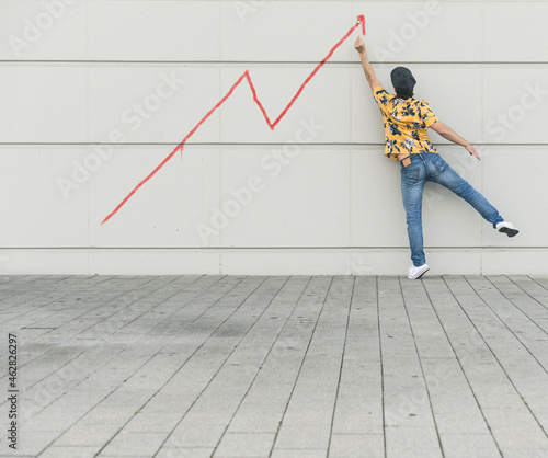 Digital composite of young man drawing a line graph at a wall photo