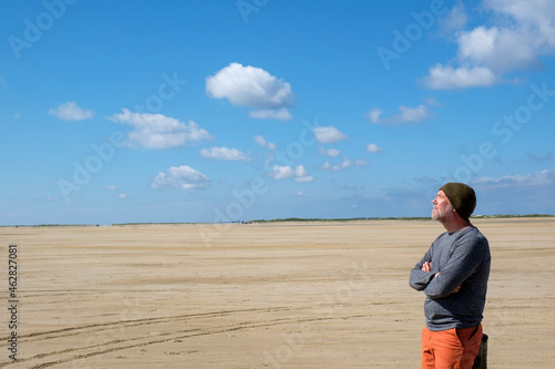 Thoughtful mature man standing at beach against blue sky on sunny day photo