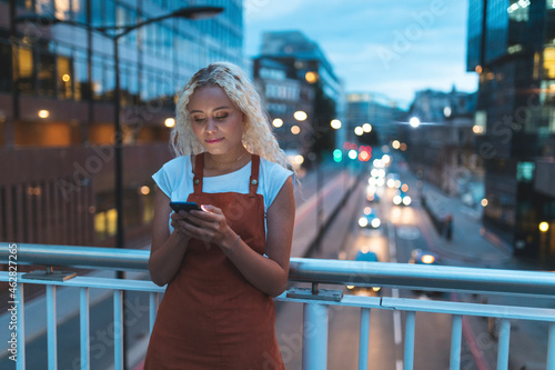Young woman in the city at dusk looking at her smartphone photo