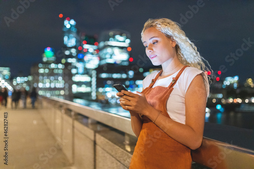 Young woman in London at night looking at her smartphone photo
