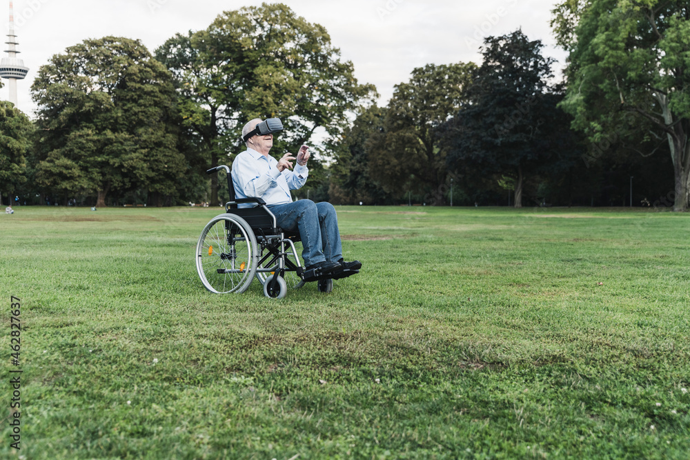 Senior man sitting in wheelchairin a park using Virtual Reality Glasses