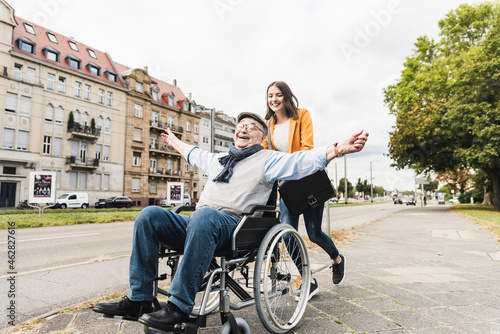 Smiling young woman pushing happy senior man in wheelchair photo