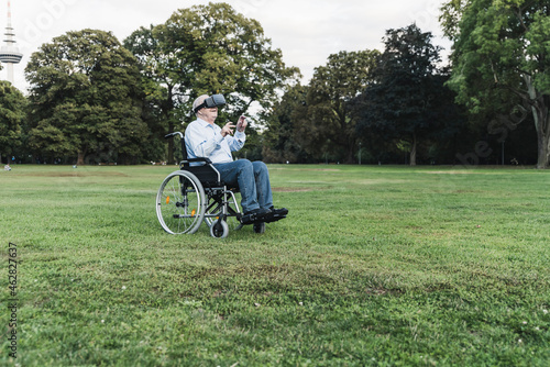 Senior man sitting in wheelchairin a park using Virtual Reality Glasses