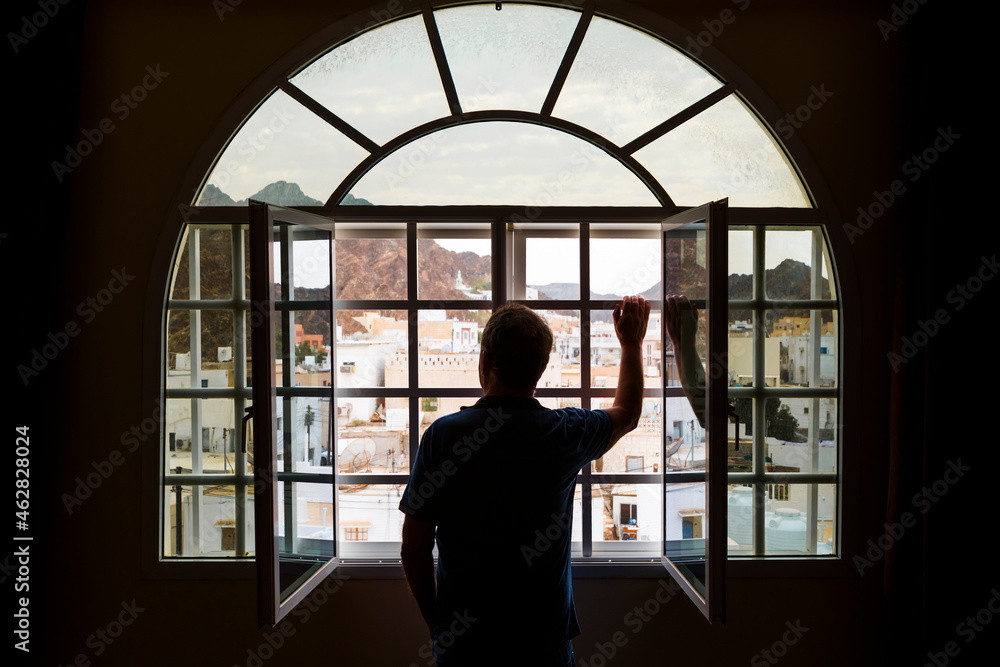 Man standing looking out of open window, Mutrah, Oman Man standing looking out of open window, Mutrah, Oman