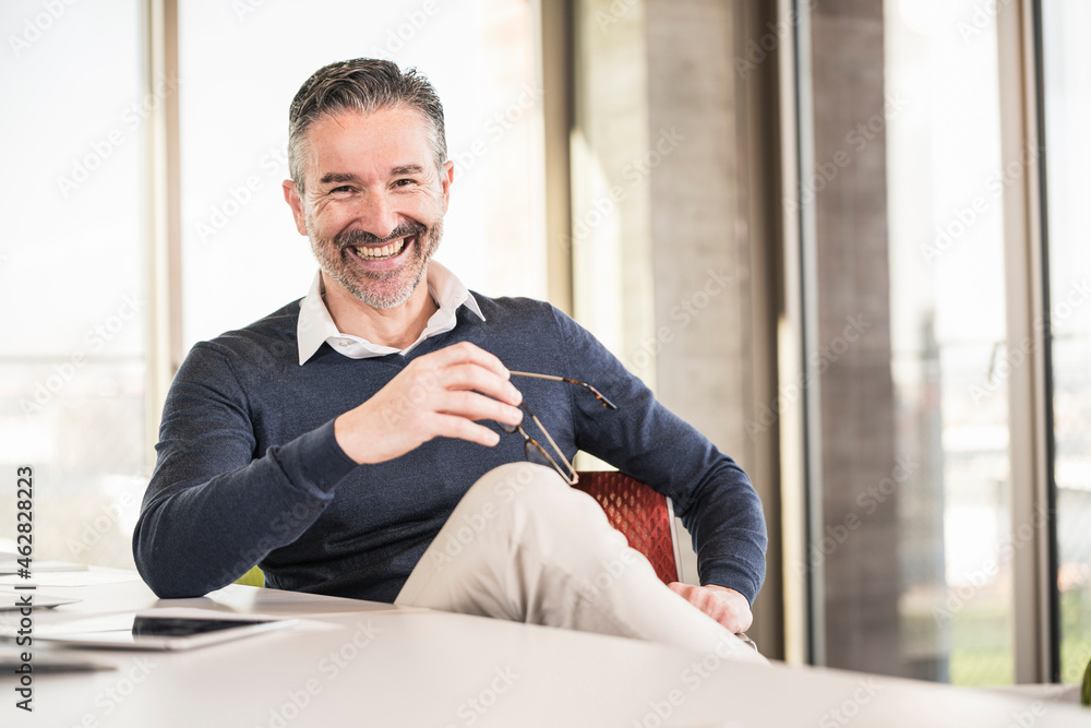 Portrait of a happy mature businessman sitting at desk in office Portrait of a happy mature businessman sitting at desk in office