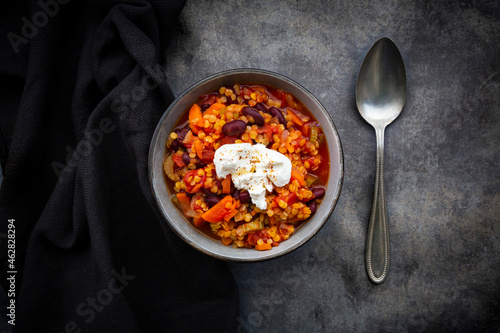 Bowl of vegetarian chili with red lentils, kidney beans, tomatoes, carrots, celery and sour cream
