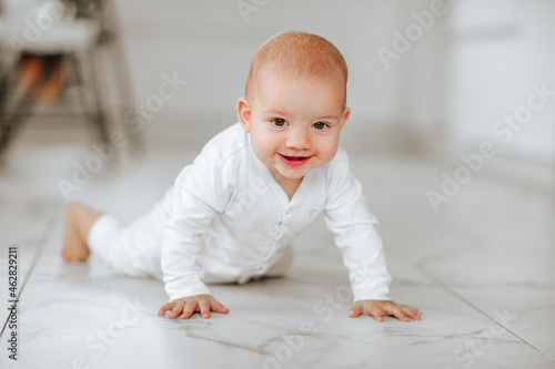 Newborn baby girl in white body growling on white warm floor at home