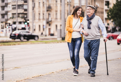 Adult granddaughter assisting her grandfather strolling with walking stick photo