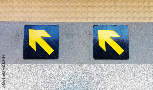 Close-up view of black arrows and yellow squares on the floor , Abstract pattern on concrete surface, Direction from train to platform, Shadow on the direction signs at the train station 