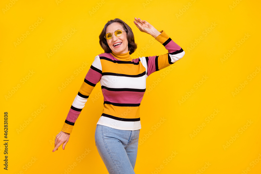 Photo of funky white hairdo aged lady dance wear eyewear striped sweater jeans isolated on yellow color background Photo of funky white hairdo aged lady dance wear eyewear striped sweater jeans isolated on yellow color background