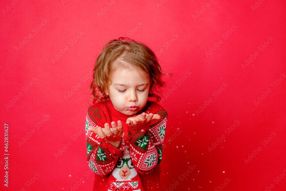 little girl in a sweater with reindeer blowing snow on a red background, christmas, new year little girl in a sweater with reindeer blowing snow on a red background, christmas, new year