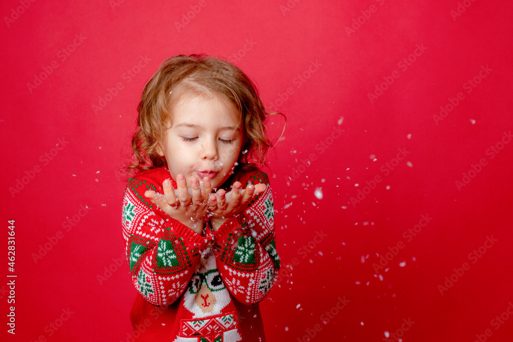 little girl in a sweater with reindeer blowing snow on a red background, christmas, new year little girl in a sweater with reindeer blowing snow on a red background, christmas, new year