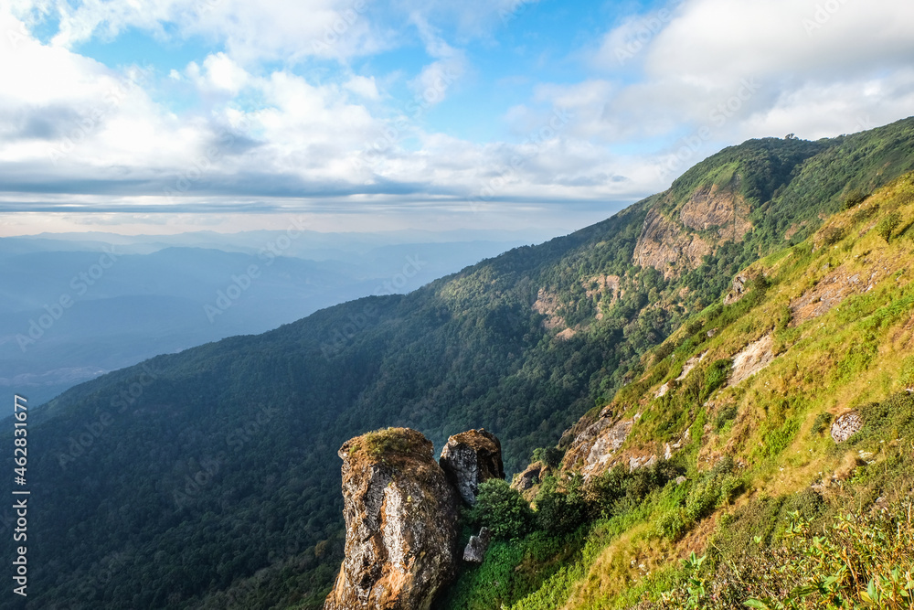 Fototapeta premium Sunlight shine on the big rocks of the hill, Adventure on the trekking trail, Sunbeam shine through the cloud to the valley and the mountain, Two boulders settle on the cliff of the mountain