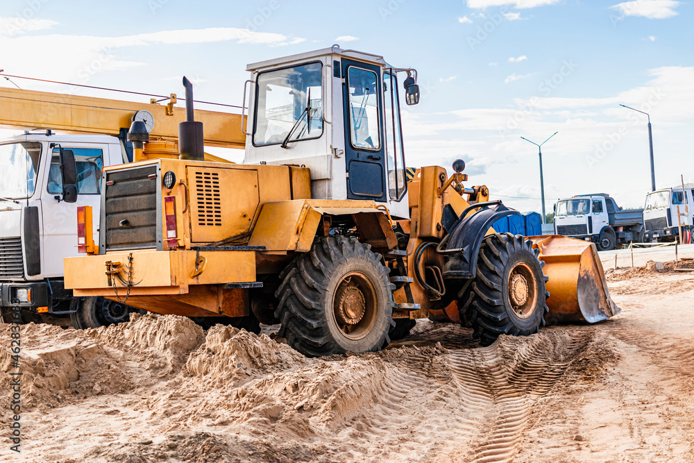 Heavy wheel loader with a bucket at a construction site. Equipment for earthworks, transportation and loading of bulk materials - earth, sand, crushed stone.