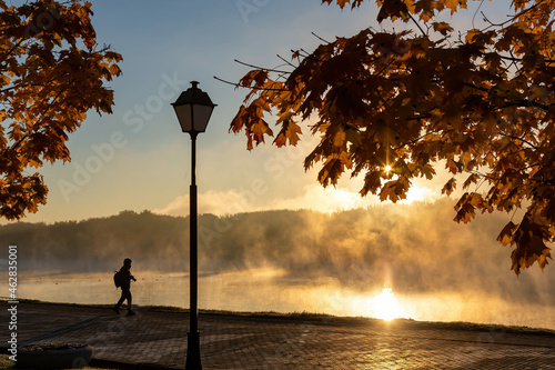 Foggy autumn dawn. Photographer in the rays of the dawn sun