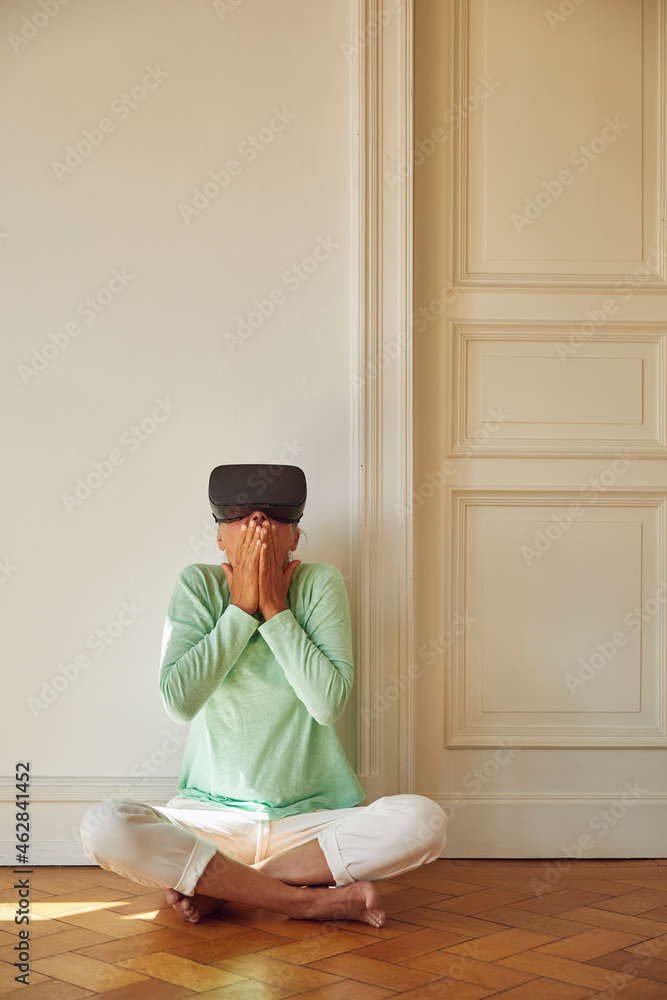 Mature woman using virtual reality simulator while sitting on floor at home Mature woman using virtual reality simulator while sitting on floor at home
