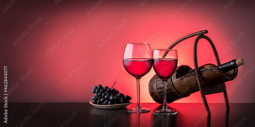Two wine glasses with red wine and bottle of wine on the table on red background with copy space. Banner. Two wine glasses with red wine and bottle of wine on the table on red background with copy space. Banner.
