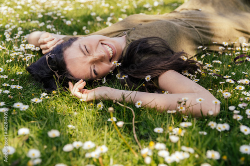 Happy woman enjoying her free time while lying on grass with daisies