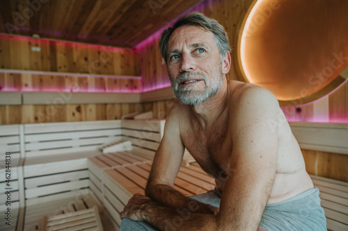 Mature man with blue eyes looking away while sitting at finnish sauna photo