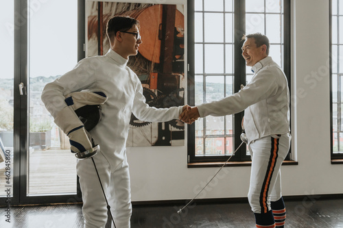 Father and son shaking hands after fencing in loft photo
