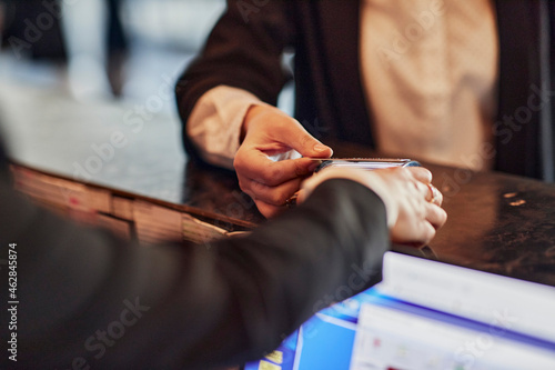 Close-up of woman paying contactless with credit card at reception desk photo