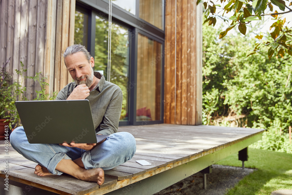 Bearded man using laptop while sitting outside house Bearded man using laptop while sitting outside house