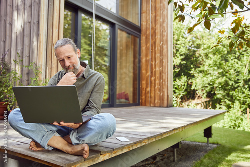 Bearded man using laptop while sitting outside house