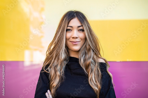 Beautiful woman with long hair smiling while standing against wall photo