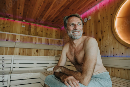 Smiling mature man looking away while sitting at finnish sauna