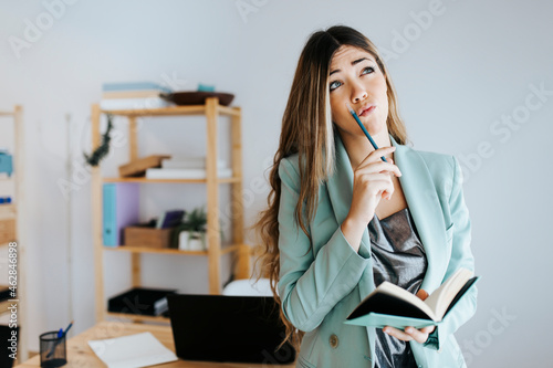 Businesswoman thinking while writing in diary at office photo