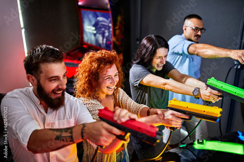 Happy friends playing and shooting with pistols in an amusement arcade photo