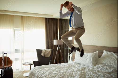 Excited businessman jumping on bed in hotel room photo