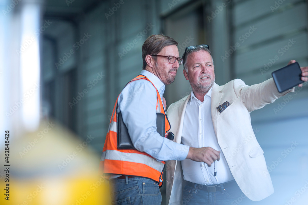 Man in reflective and businessman with cell phone talking in industrial hall Man in reflective and businessman with cell phone talking in industrial hall