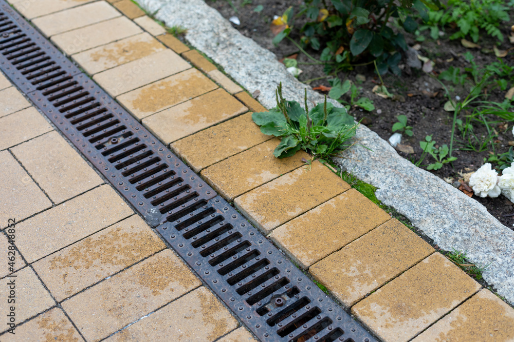 Grating of drainage system rainwater in the park at the sidewalk from a stone yellow paving slabs - obrazy, fototapety, plakaty 