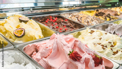 Fotografia Multi colored Italian ice cream gelato with various fruit flavors decorated with fruits, nuts or chocolate  in the refrigerator-display case