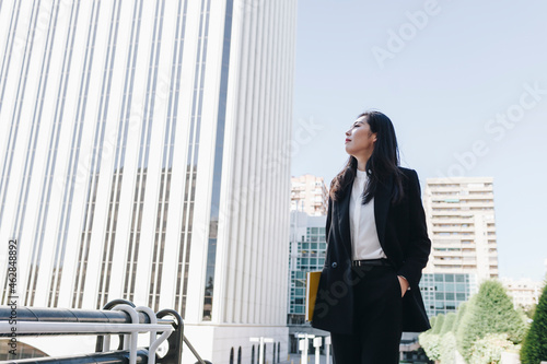 Businesswoman with hands in pockets wearing blazer jacket while standing against financial district photo