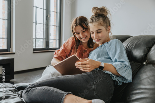 Friends using digital tablet while relaxing on sofa at home photo