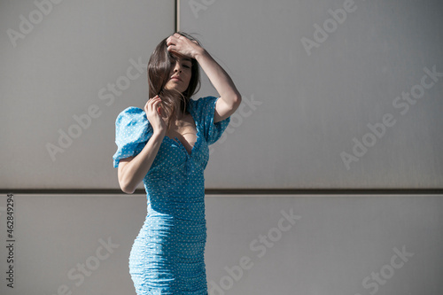 Beautiful young woman in blue mini dress standing against gray wall