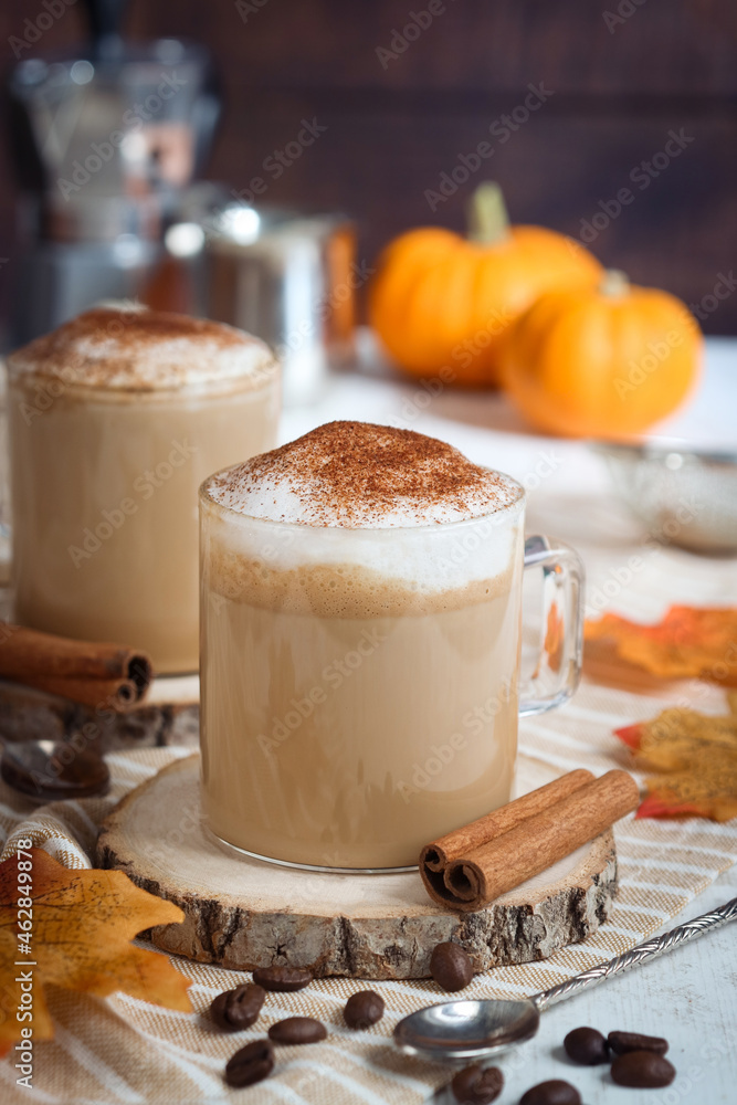 A glass of hot  autumn drink pumpkin spice latte in alternate healthy way without whip cream with mousse of milk topped with ground spices. Jack-Be-Little squad in background, with coffee bean - obrazy, fototapety, plakaty 